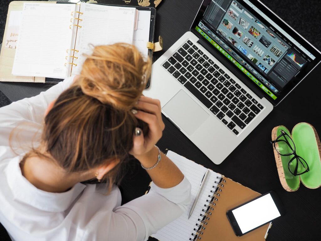 pexels-photo-313690 Overhead view of a stressed woman working at a desk with a laptop, phone, and notebooks.